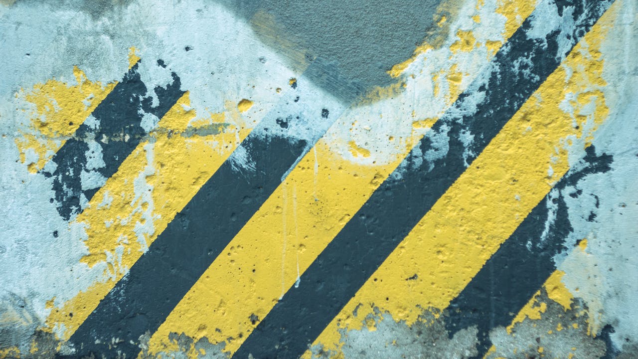 Close-up of weathered and chipped paint on a wall revealing yellow and black stripes.